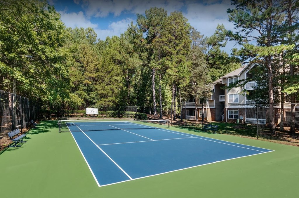 a tennis court with trees and a house in the background