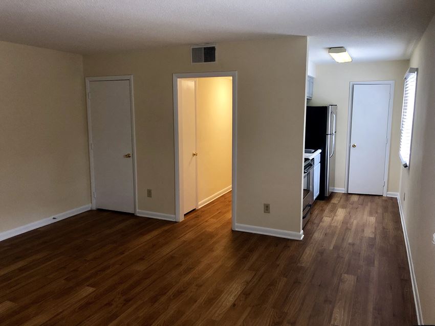 an empty living room with wood floors and a kitchen