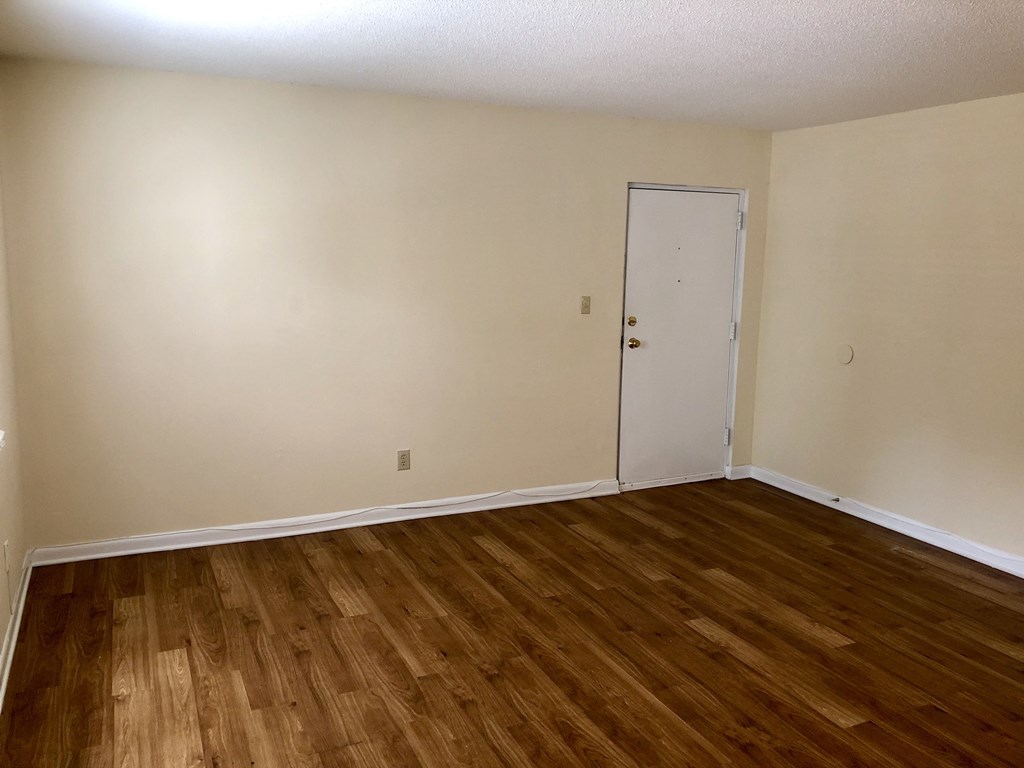 an empty living room with wooden floors and a white door