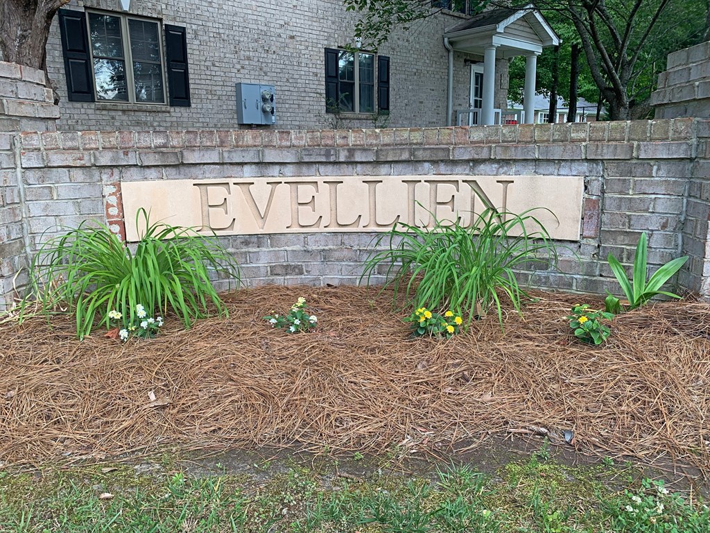 a sign in front of a brick wall with plants and flowers