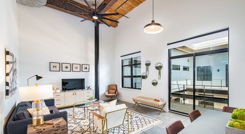 A living room with a dark blue sofa, a wooden coffee table, and a TV on the wall at Judson Mill Lofts and The Jenny & Westervelt in Greenville, SC