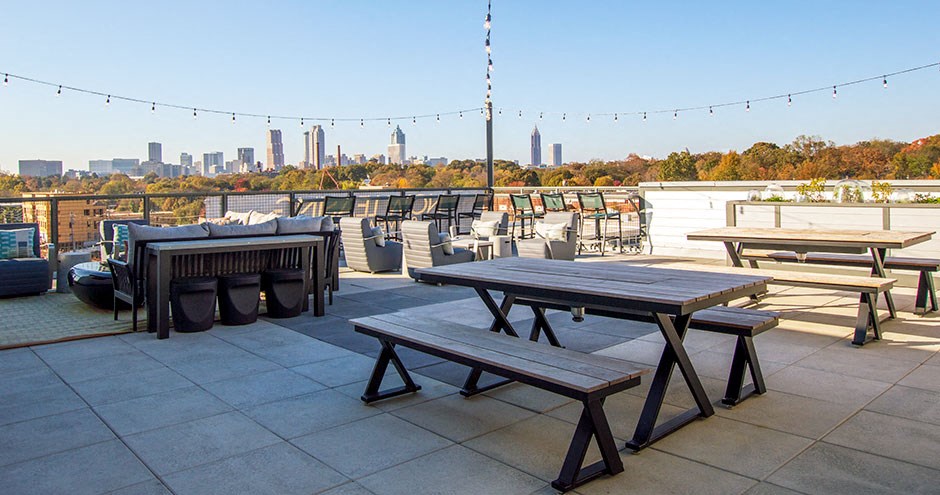 a rooftop patio with picnic tables and a city in the background