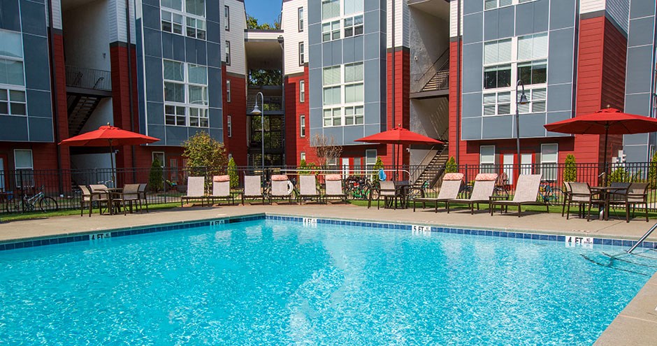 a swimming pool with chairs and umbrellas in front of apartment buildings