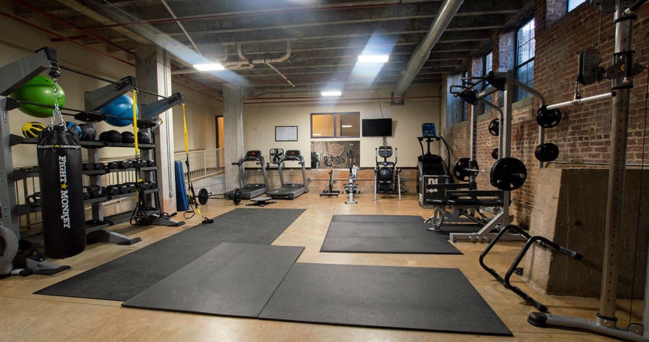 a gym with mats and weights on the floor and a brick wall
