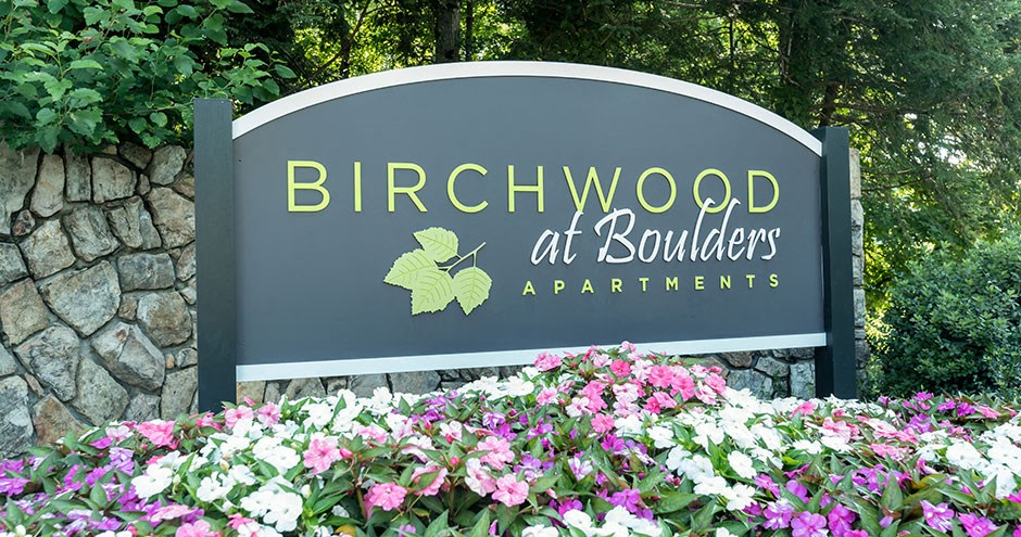 a sign for birchwood at boulevard apartments with flowers in front of it