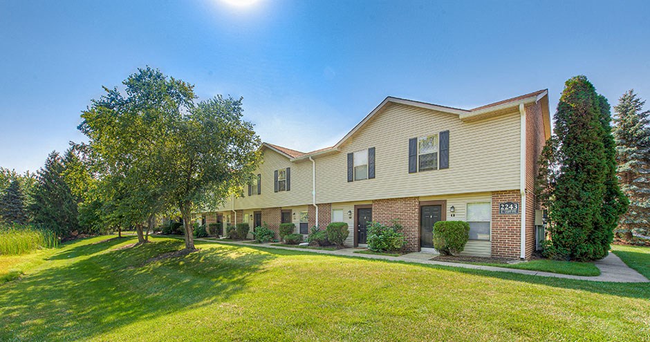 a yellow house with a green lawn and trees