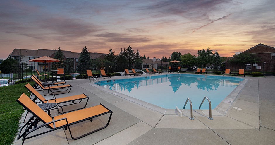 a swimming pool with chairs around it at sunset