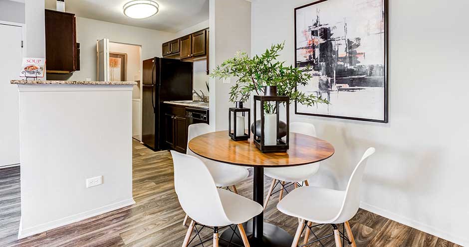 a room with a table and chairs and a kitchen in the background
