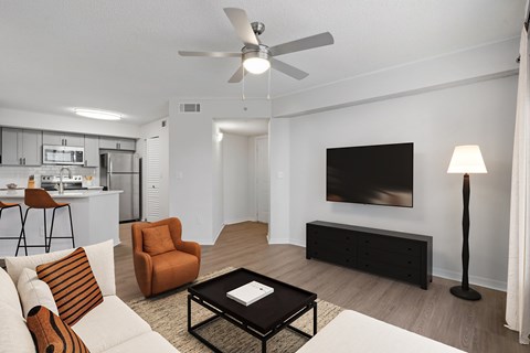 A living room with a white couch, a black coffee table, and a television on the wall.