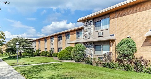 a brick apartment building with a green lawn and walkway