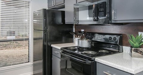 A black refrigerator is in a kitchen with a stove and microwave above it.
