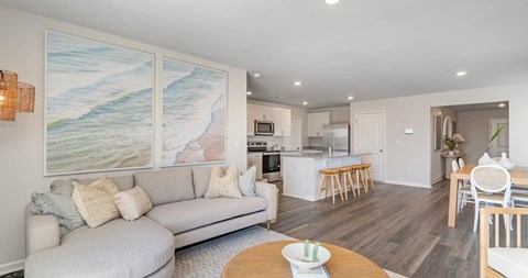 A living room with a grey couch and a painting of a beach on the wall.