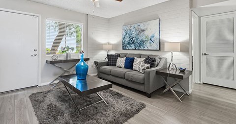A living room with a grey couch, a blue vase, and a painting on the wall.