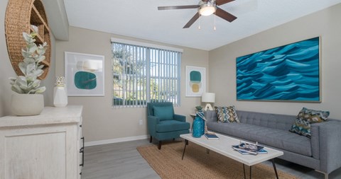 A living room with a grey couch, a blue chair, and a painting on the wall.
