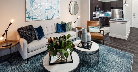 A living room with a grey couch, a round table with a plant on it, and a painting on the wall.