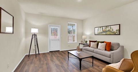 A living room with a grey couch, a wooden floor, and a painting on the wall.