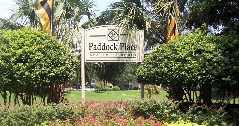 a sign for paddock place in a park with trees