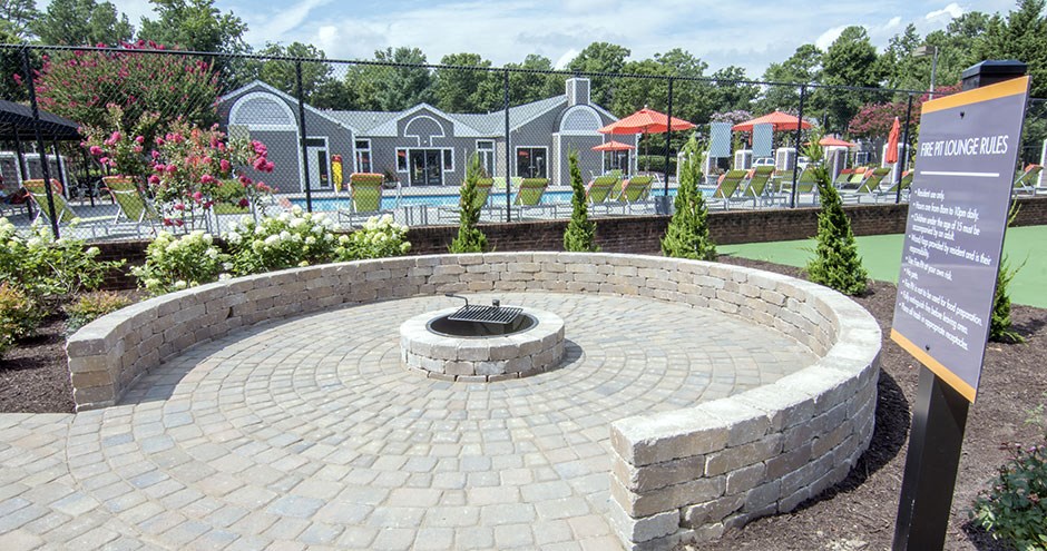 a brick fire pit in a park with a pool and houses in the background