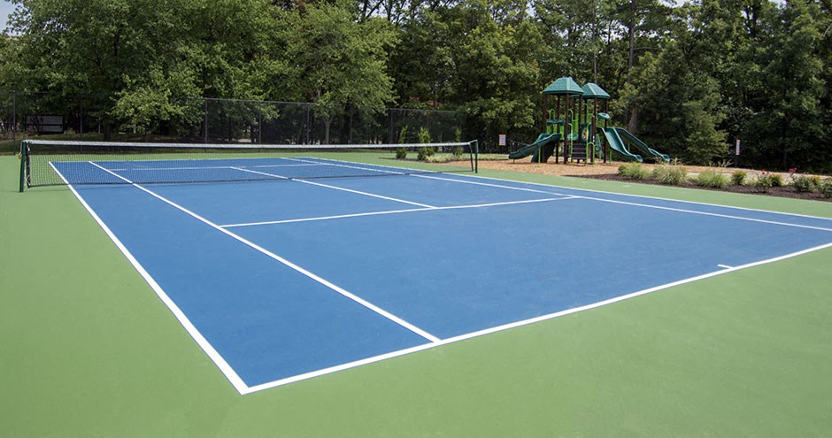 a blue and green tennis court with a playground in the background