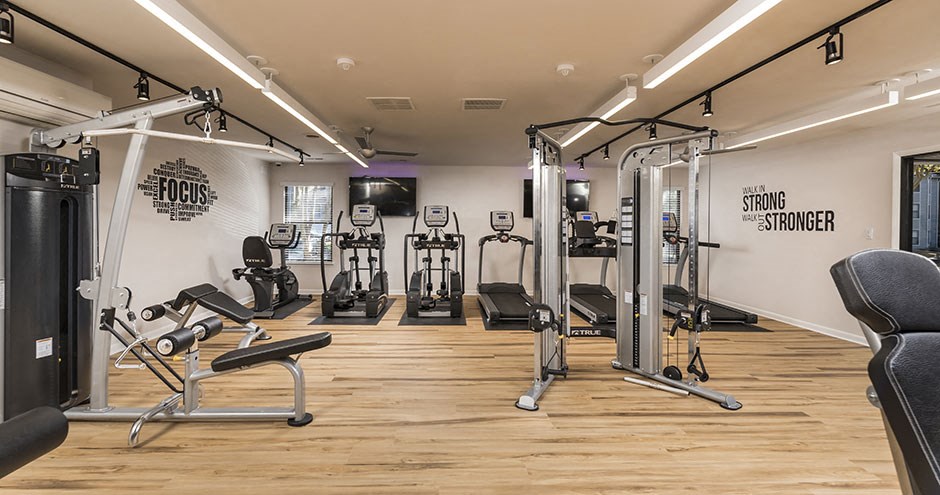 a gym with cardio equipment and weights on a wood floor