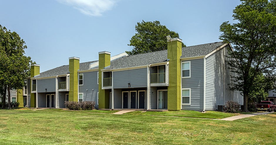 a gray house with green pillars and a lawn