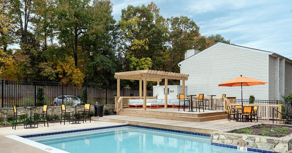 a swimming pool and patio with chairs and an umbrella next to a house