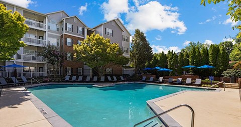 A swimming pool surrounded by lounge chairs and umbrellas in front of apartment buildings.