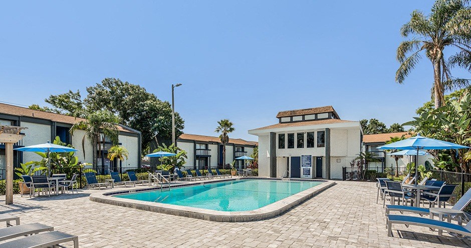 a swimming pool with lounge chairs and umbrellas in front of a building