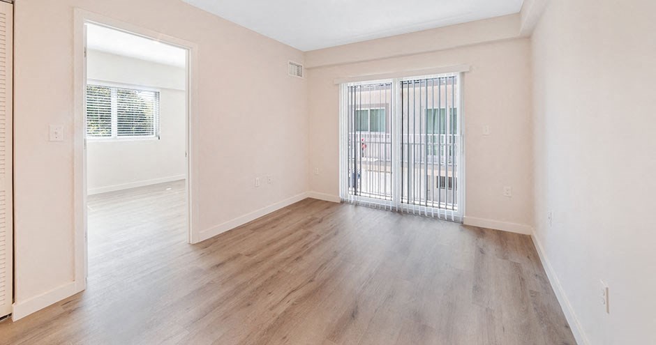 an empty living room with a sliding glass door to a balcony