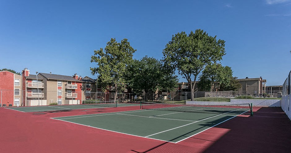 a tennis court with trees and apartments in the background