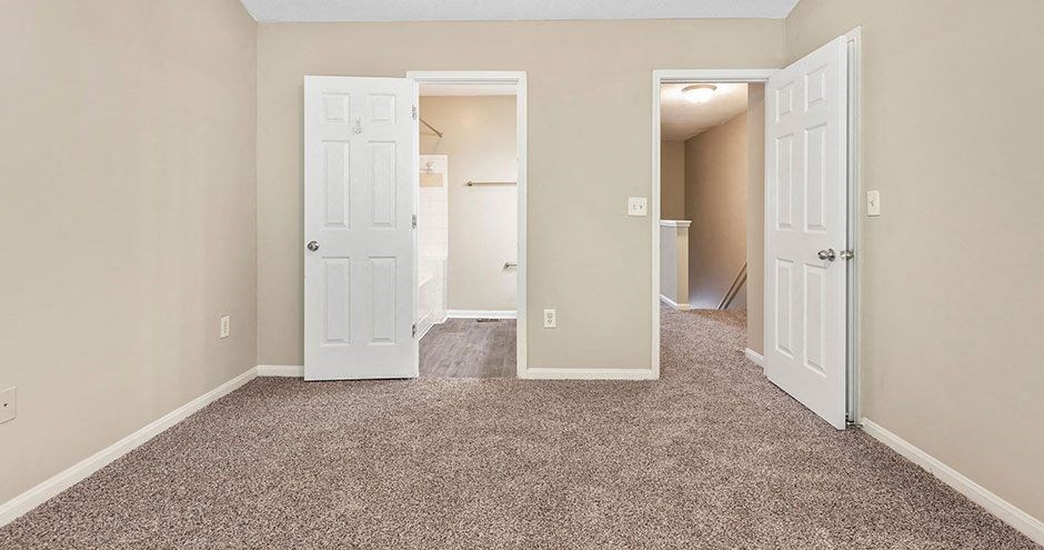 an empty bedroom with two doors and a carpeted floor