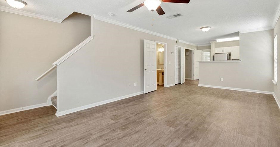 an empty living room with a kitchen and a ceiling fan