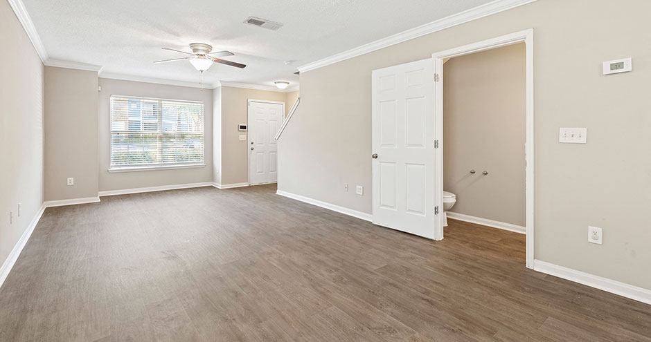 an empty living room with a ceiling fan and a white door