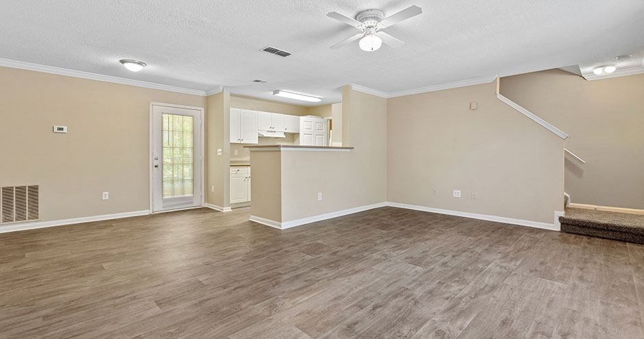 an empty living room with a kitchen and a ceiling fan
