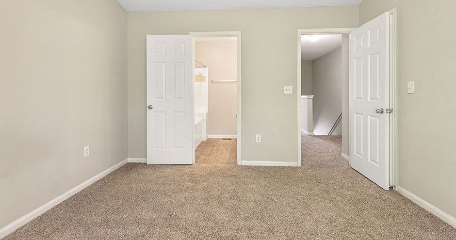 an empty bedroom with two doors and a carpeted floor
