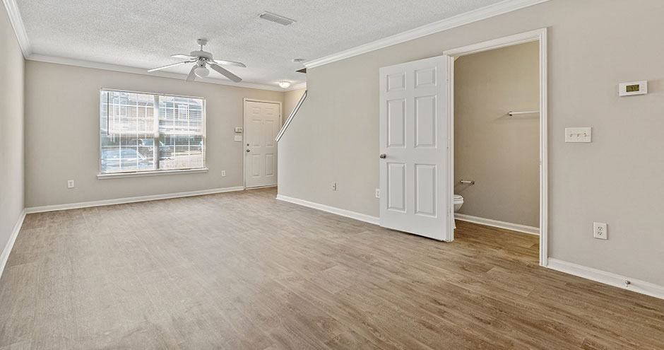 an empty living room with a ceiling fan and a white door