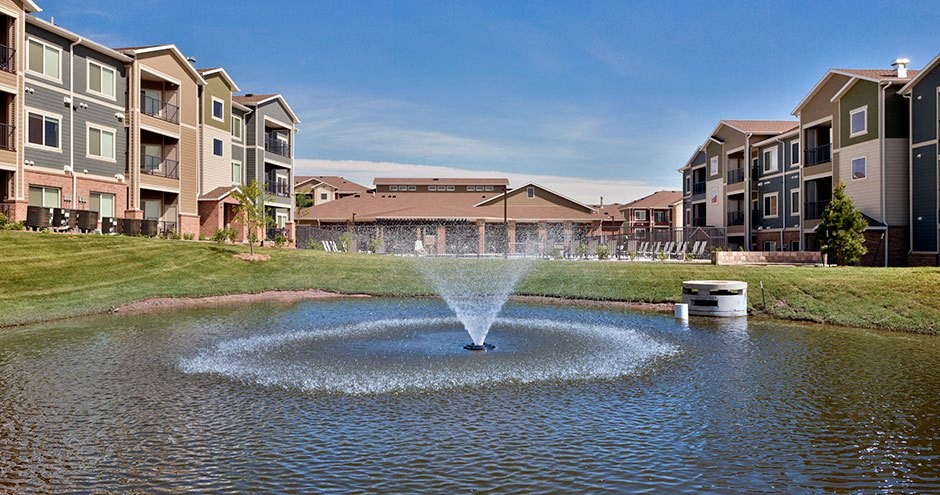 a fountain in the middle of a pond in front of an apartment building