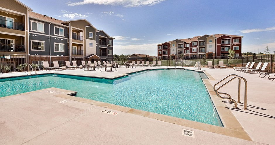 a swimming pool with chairs in front of an apartment building