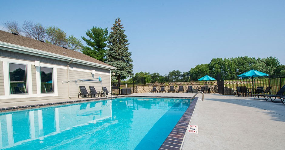 the pool is next to a house with chairs and umbrellas