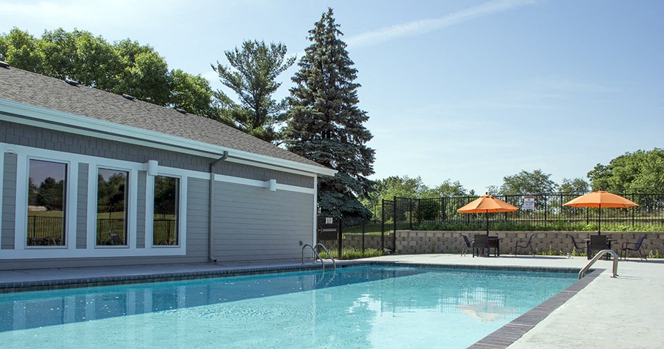 a swimming pool in front of a house with a patio and umbrellas