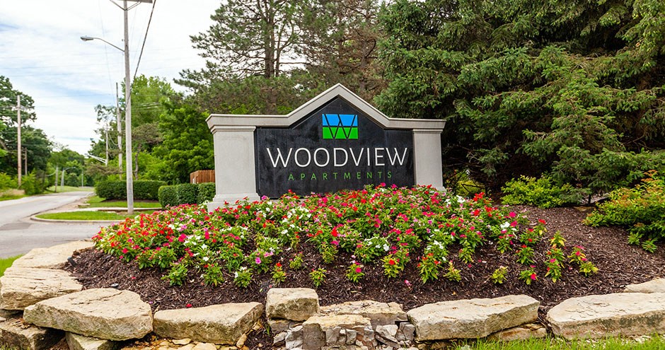 a sign for woodview apartments in front of a flower garden
