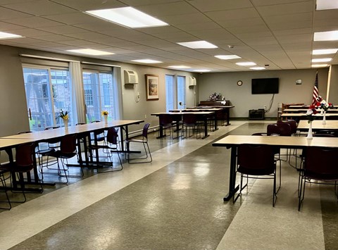 A conference room with tables and chairs and a television on the wall.