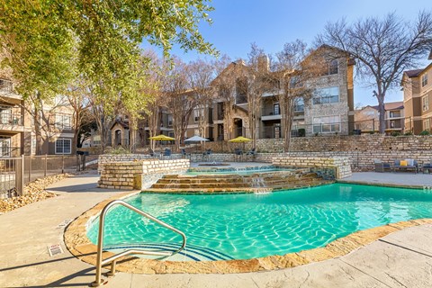 A swimming pool surrounded by a stone wall and a metal railing.