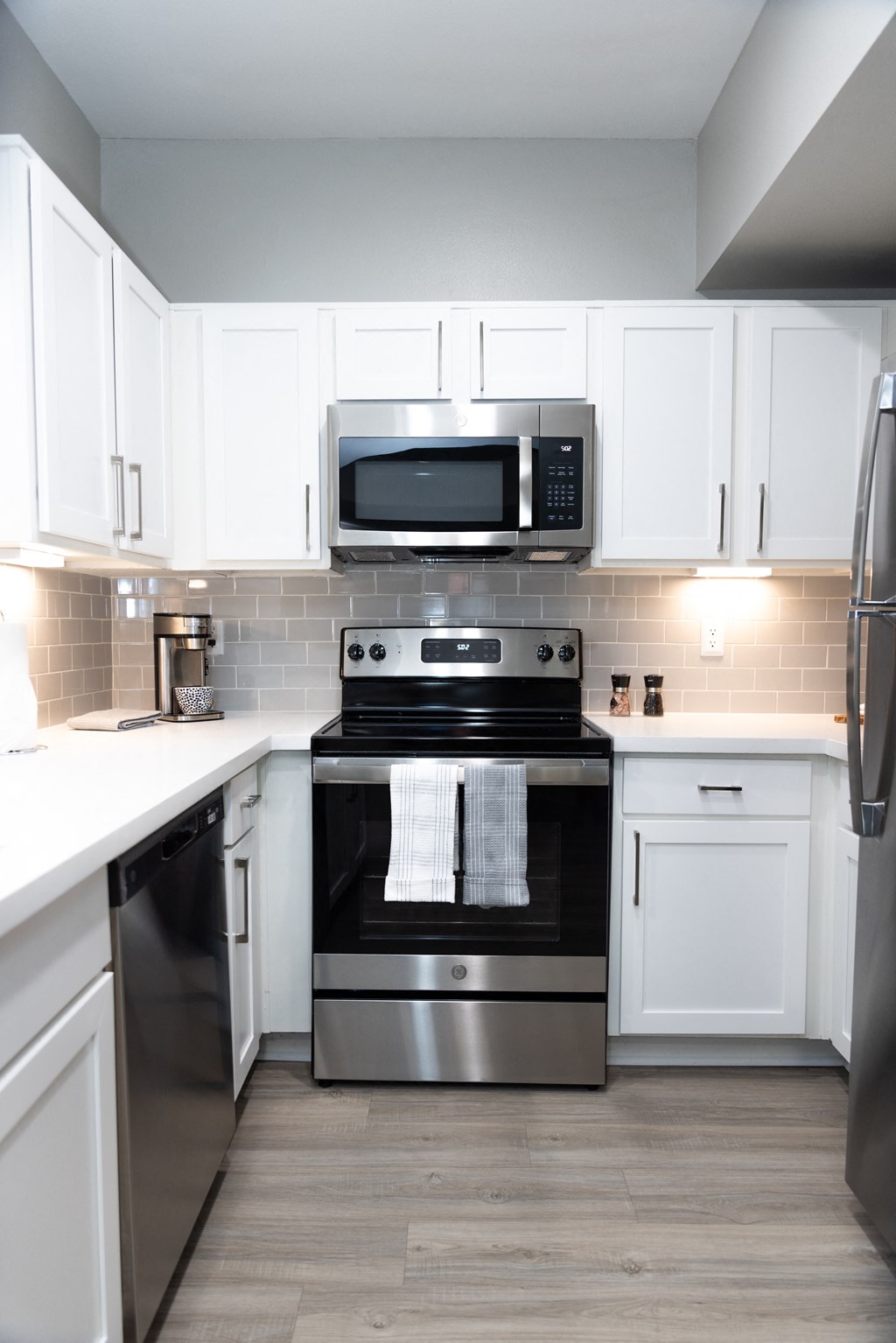Pet-Friendly Apartments in Tanglewood, Houston, TX - Crosley Tanglewood - Modern Kitchen with Stainless Steel Appliances Including Oven, Refridgerator, Microwave, and Dishwasher, with White Countertops, White Cabinetry, Grey Tile Backsplash, and Light Wood Floor