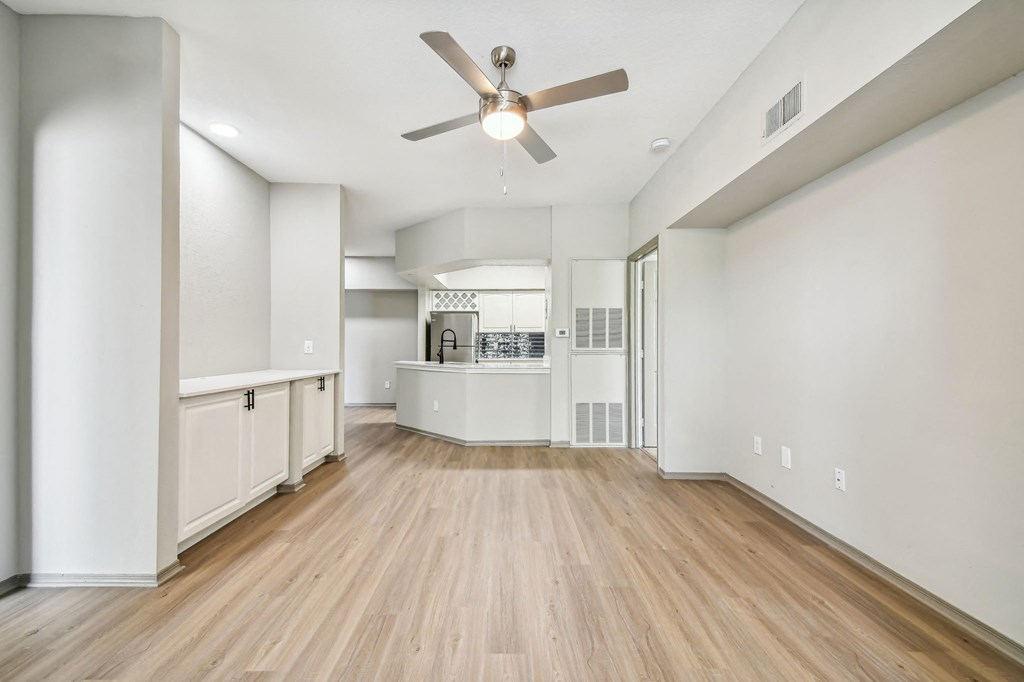 an empty living room with a ceiling fan and a kitchen