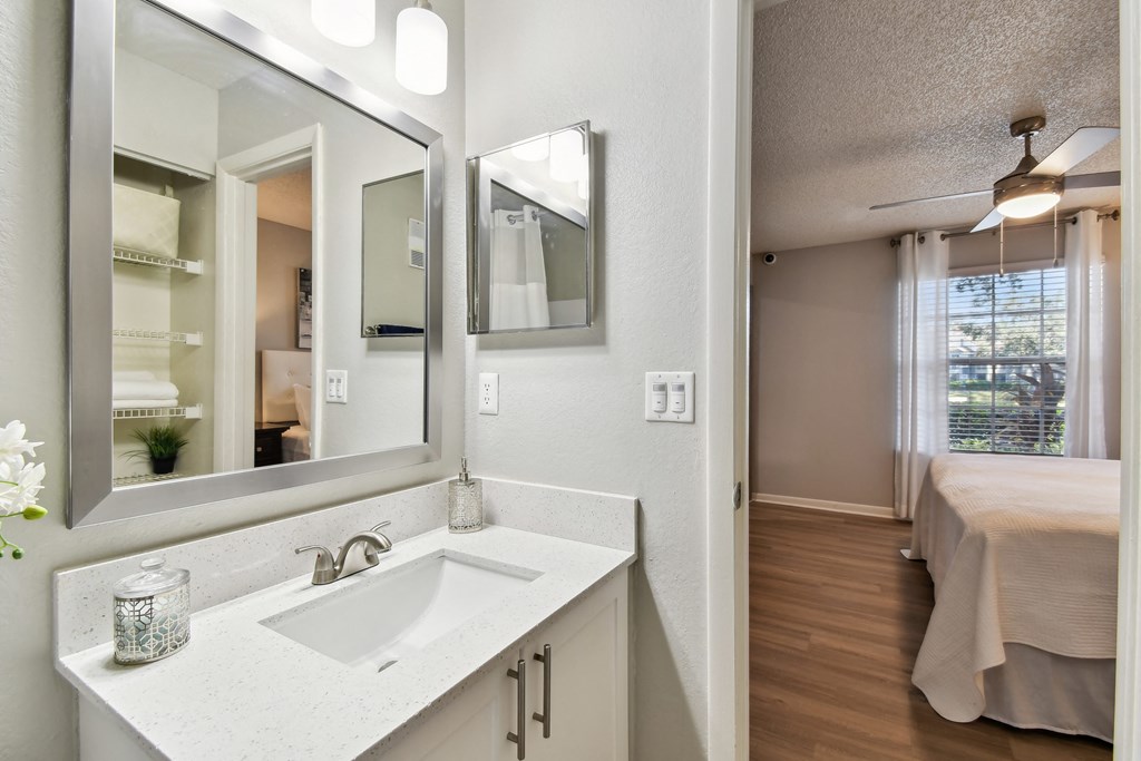 a bathroom with a sink and a mirror and a bedroom with a bed