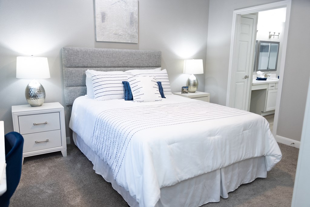 1 BR Apartments in Tanglewood, Houston, TX - Crosley Tanglewood -Furnished Bedroom with Bed, Carpeted Floor, White Nightstands, Lamps, Desk, and Attached Bathroom