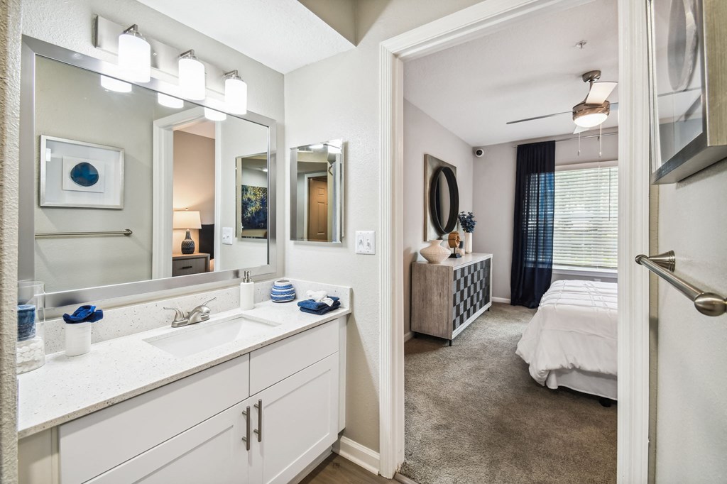 a bathroom with a sink and a mirror and a bedroom with a bed