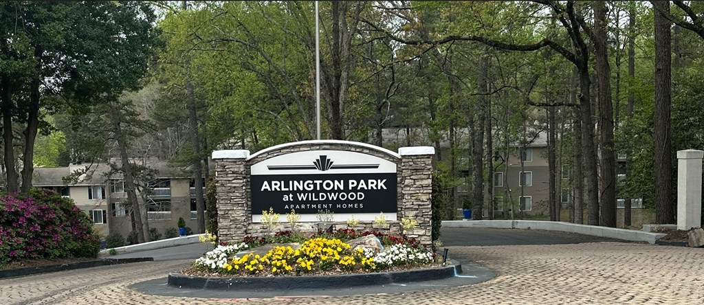 a sign in front of a park with trees and flowers