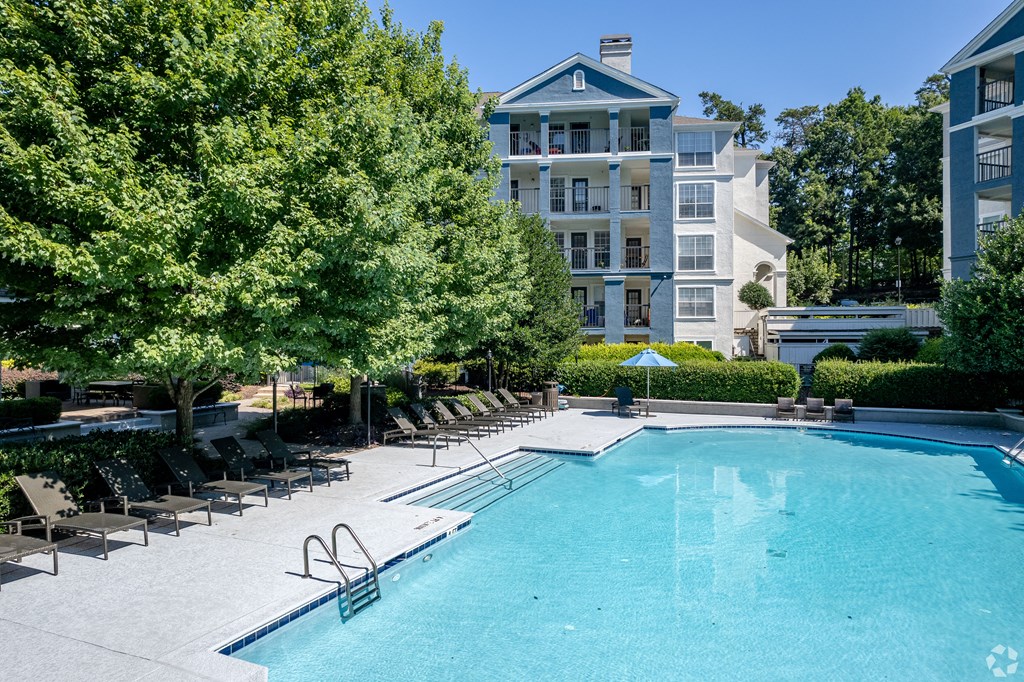 a swimming pool with chaise lounge chairs and trees in front of an apartment building
